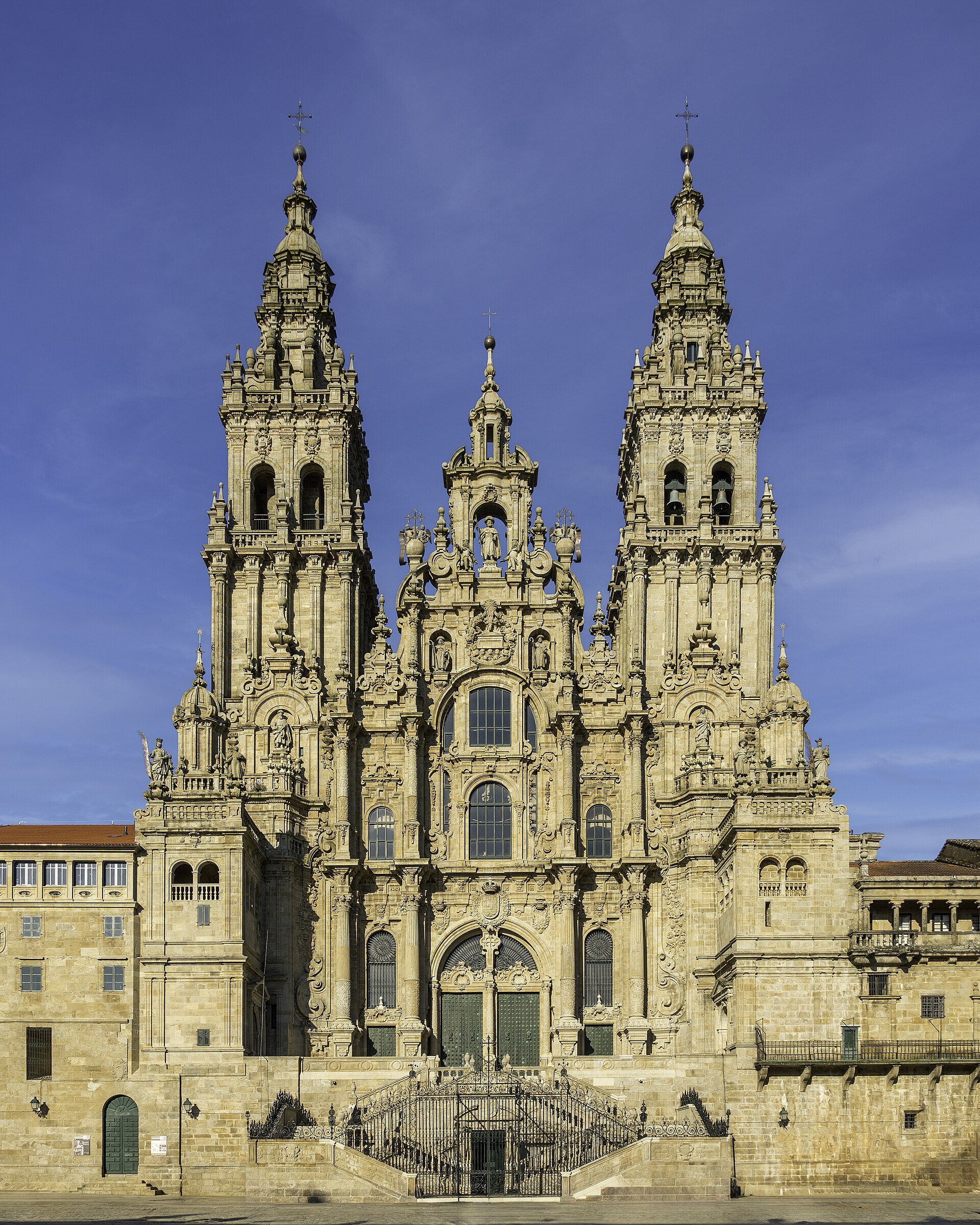 Fachada del Obradoiro de la catedral de Santiago de Compostela, con reja y dos torres, cielo azul.